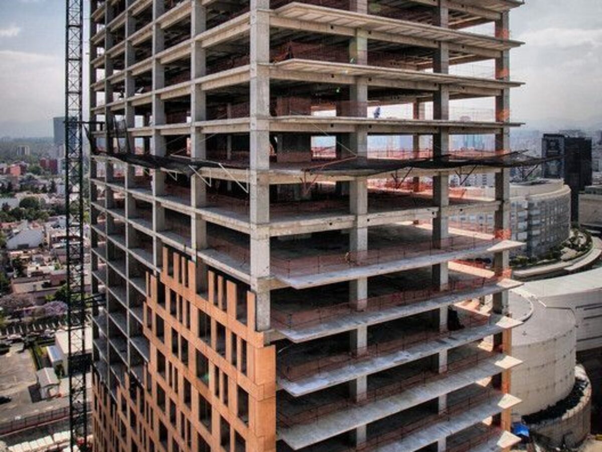 Torre residencial em obra, estrutura de concreto aparente e guindaste, com a cidade ao fundo